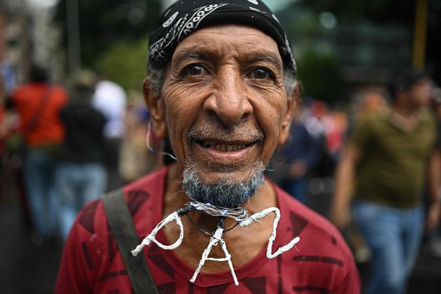 A supporter of Venezuela's President Nicolas Maduro sports a decorated beard during a march to commemorate the "Day of Indigenous Resistance" in Caracas on October 12, 2025. On Sunday, Venezuelan President Nicolбs Maduro called opposition leader Marнa Corina Machado a “demonic witch,” two days after she was awarded the Nobel Peace Prize. (Photo by Federico PARRA / AFP)