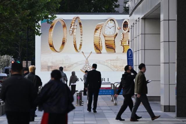 People walk near a screen advertisement promoting jewellery in Beijing on October 13, 2025. (Photo by GREG BAKER / AFP)
