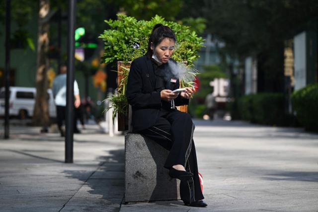 A woman smokes outside a shopping mall in Beijing on October 13, 2025. (Photo by GREG BAKER / AFP)