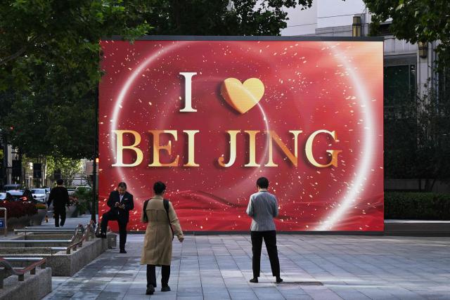 People stand near a slogan on a screen outside a shopping mall in Beijing on October 13, 2025. (Photo by GREG BAKER / AFP)