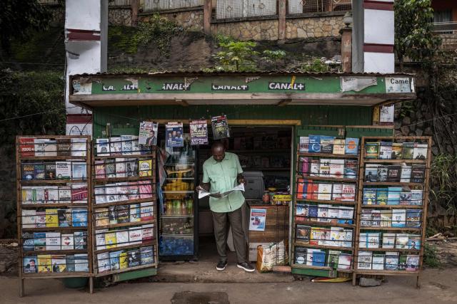 The owner of a kiosk reads a newspaper at the entrance of his shop in Yaounde, on October 13, 2025 a day following Cameroon's presidential election. (Photo by MARCO LONGARI / AFP)
