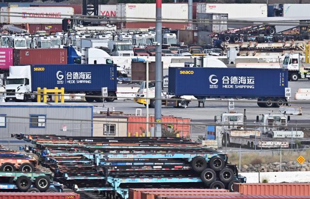 Container trucks from Hede Shipping, from the Chinese state-owned Hebei Port Group, pass a row of flatbed trailers at the Port of Los Angeles in Los Angeles, California on October 13, 2025. President Donald Trump said October 12, 2025 the United States wants to help China, not hurt it, striking a conciliatory tone days after threatening an additional 100 percent tariff on the world's second-largest economy. Trump's statements on October 10 as well as his threat to cancel a meeting with Xi later this month sent Wall Street stocks tumbling into negative territory as traders worried the trade war between Washington and Beijing could reignite. (Photo by Frederic J. BROWN / AFP)