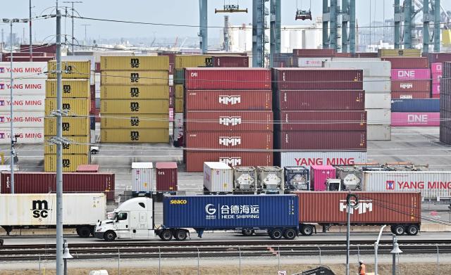 A container truck from Hede Shipping, from the Chinese state-owned Hebei Port Group, passes containers stacked at the Port of Los Angeles in Los Angeles, California on October 13, 2025. President Donald Trump said October 12, 2025 the United States wants to help China, not hurt it, striking a conciliatory tone days after threatening an additional 100 percent tariff on the world's second-largest economy. Trump's statements on October 10 as well as his threat to cancel a meeting with Xi later this month sent Wall Street stocks tumbling into negative territory as traders worried the trade war between Washington and Beijing could reignite. (Photo by Frederic J. BROWN / AFP)