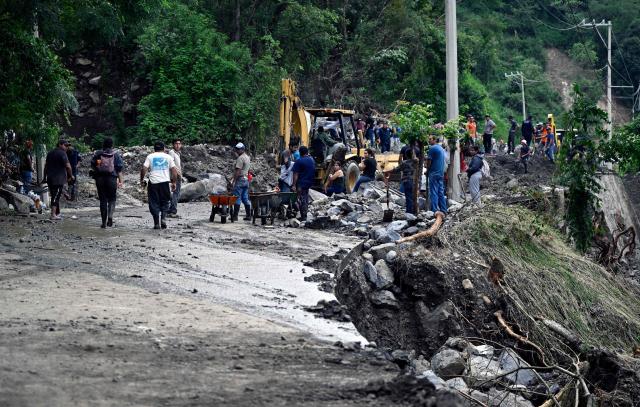 Locals clean and remove mud from a landslide at the entrance to the town of San Bartolo Tutotepec in Hidalgo state, Mexico, on October 13, 2025. The death toll from flooding in central and eastern Mexico -mostly in the Veracruz, Hidalgo and Puebla states- has risen sharply to at least 64, with another 65 still missing, authorities reported. (Photo by Alfredo ESTRELLA / AFP)