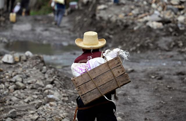 A local walks past a landslide at the entrance to the town of San Bartolo Tutotepec in Hidalgo state, Mexico, on October 13, 2025. The death toll from flooding in central and eastern Mexico -mostly in the Veracruz, Hidalgo and Puebla states- has risen sharply to at least 64, with another 65 still missing, authorities reported. (Photo by Alfredo ESTRELLA / AFP)