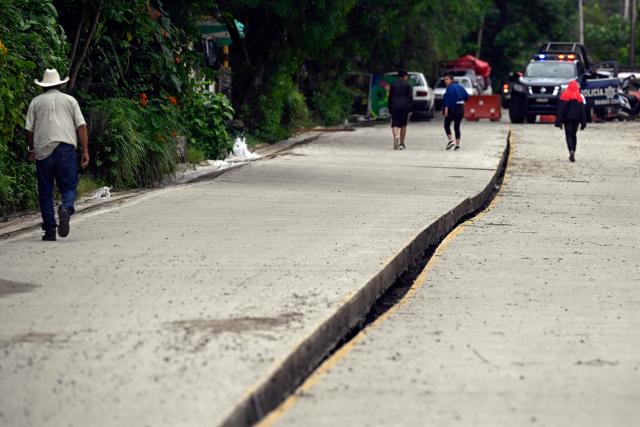 People walk along a damaged asphalt road following heavy rains in San Bartolo Tutotepec, Hidalgo state, Mexico, on October 13, 2025. The death toll from flooding in central and eastern Mexico -mostly in the Veracruz, Hidalgo and Puebla states- has risen sharply to at least 64, with another 65 still missing, authorities reported. (Photo by Alfredo ESTRELLA / AFP)