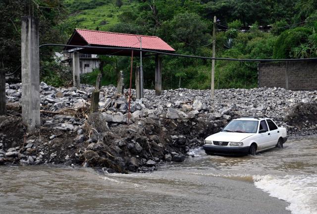 A car drives through a flooded street after a river overflowed in San Bartolo Tutotepec, Hidalgo state, Mexico, on October 13, 2025. The death toll from flooding in central and eastern Mexico -mostly in the Veracruz, Hidalgo and Puebla states- has risen sharply to at least 64, with another 65 still missing, authorities reported. (Photo by Alfredo ESTRELLA / AFP)