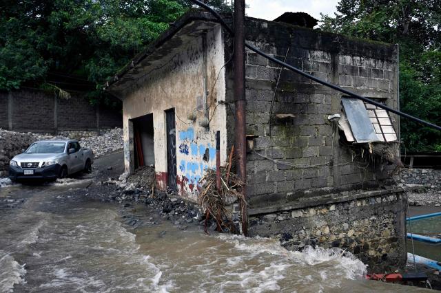 A car drives through a flooded street after a river overflowed in San Bartolo Tutotepec, Hidalgo state, Mexico, on October 13, 2025. The death toll from flooding in central and eastern Mexico -mostly in the Veracruz, Hidalgo and Puebla states- has risen sharply to at least 64, with another 65 still missing, authorities reported. (Photo by Alfredo ESTRELLA / AFP)