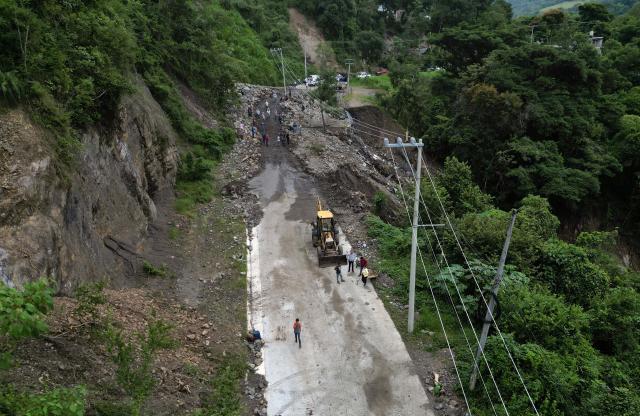 This aerial view shows residents cleaning up and removing mud after a landslide at the entrance to the town of San Bartolo Tutotepec in Hidalgo state, Mexico, on October 13, 2025. The death toll from flooding in central and eastern Mexico -mostly in the Veracruz, Hidalgo and Puebla states- has risen sharply to at least 64, with another 65 still missing, authorities reported. (Photo by Alfredo ESTRELLA / AFP)