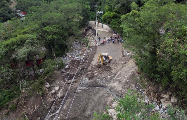 This aerial view shows residents cleaning up and removing mud after a landslide at the entrance to the town of San Bartolo Tutotepec in Hidalgo state, Mexico, on October 13, 2025. The death toll from flooding in central and eastern Mexico -mostly in the Veracruz, Hidalgo and Puebla states- has risen sharply to at least 64, with another 65 still missing, authorities reported. (Photo by Alfredo ESTRELLA / AFP)