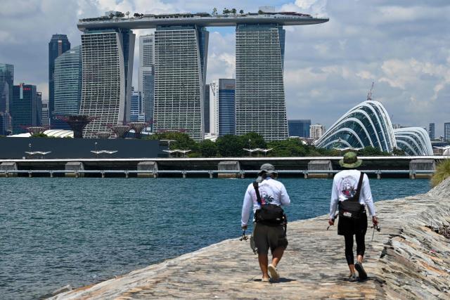 Anglers walk along a breakwater as the Marina Bay Sands and city skyline is seen from Marina East in Singapore on October 14, 2025. (Photo by Roslan RAHMAN / AFP)