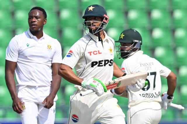 Pakistan's captain Shan Masood (C) and teammate Abdullah Shafique (R) run between the wickets as South Africa's Kagiso Rabada watches during the third day of the first Test cricket match between Pakistan and South Africa at the Gaddafi Stadium in Lahore on October 14, 2025. (Photo by Aamir QURESHI / AFP)