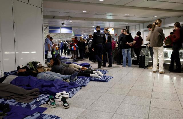 (FILES) Passengers sleep on inflatable mattresses on the ground while others queue up next to them at Munich International Airport in Munich, southern Germany, on early October 4, 2025, after reports of drone sightings again forced Munich airport to close and more than 30 flights had to be cancelled and left nearly 3,000 passengers stranded. Once holidaymakers took off from here, but today an ex-Soviet airfield is a testing ground for ways to take down the drones increasingly buzzing through German skies. Germany has been rattled by a spate of mysterious sightings of unmanned aerial vehicles (UAVs), believed to be from Russia, over military bases, industrial sites and an airport. But at the airstrip near the eastern city of Magdeburg, researchers of the German Aerospace Center (DLR) have been testing more subtle options to deal with potentially hostile drones. (Photo by Michaela STACHE / AFP)