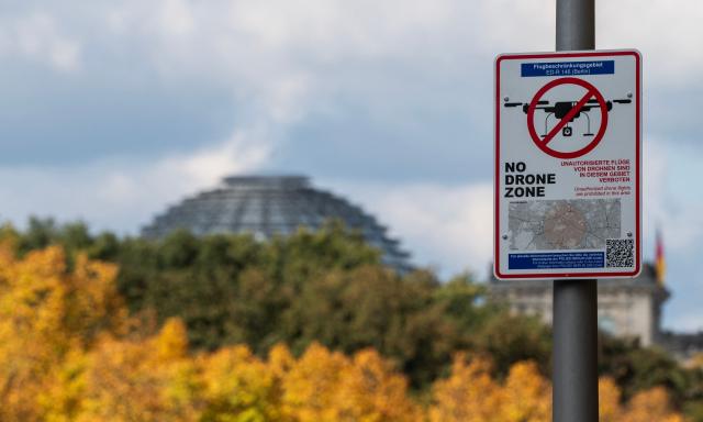 (FILES) A sign indicates the start of a "No Drone Zone" in central Berlin on October 2, 2025, as the dome of the Reichstag building is seen behind autumnal trees in the distance. Once holidaymakers took off from here, but today an ex-Soviet airfield is a testing ground for ways to take down the drones increasingly buzzing through German skies. Germany has been rattled by a spate of mysterious sightings of unmanned aerial vehicles (UAVs), believed to be from Russia, over military bases, industrial sites and an airport. But at the airstrip near the eastern city of Magdeburg, researchers of the German Aerospace Center (DLR) have been testing more subtle options to deal with potentially hostile drones. (Photo by John MACDOUGALL / AFP)