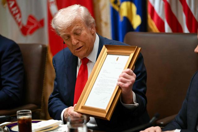 US President Donald Trump holds up a framed letter presented by Argentina's President Javier Milei in the Cabinet Room at the White House in Washington, DC on October 14, 2025. (Photo by ANDREW CABALLERO-REYNOLDS / AFP)