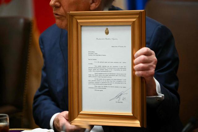 US President Donald Trump holds up a framed letter presented by Argentina's President Javier Milei in the Cabinet Room at the White House in Washington, DC on October 14, 2025. (Photo by ANDREW CABALLERO-REYNOLDS / AFP)