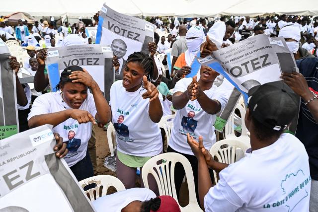 Supporters wearing T-shirts bearing the image of Democratic Congress (CODE) Presidential candidate Jean-Loui Billon dance with his posters ahead of his arrival at a campaign rally in the commune of Cocody in Abidjan on October 14, 2025. Ivory Coast Presidential election is scheduled for October 25, 2025. (Photo by Sia KAMBOU / AFP)