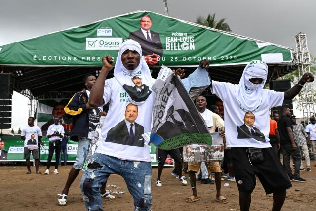 Supporters wearing T-shirts bearing the image of Democratic Congress (CODE) Presidential candidate Jean-Loui Billon dance with his posters ahead of his arrival at a campaign rally in the commune of Cocody in Abidjan on October 14, 2025. Ivory Coast Presidential election is scheduled for October 25, 2025. (Photo by Sia KAMBOU / AFP)