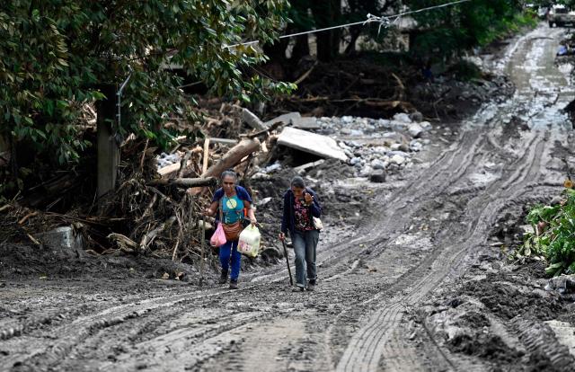 Women wade through mud after severe flooding hit the town of Huehuetla in Hidalgo state, Mexico, on October 14, 2025. Rescuers scrambled on October 13, 2025, to reach people cut off by devastating floods that have claimed 64 lives in central and eastern Mexico, with another 65 people reported missing. (Photo by Alfredo ESTRELLA / AFP)