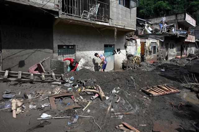 Men remove the mud after severe flooding hit the town of Huehuetla,, in Hidalgo state, Mexico on October 14, 2025. Rescuers scrambled on October 13, 2025, to reach people cut off by devastating floods that have claimed 64 lives in central and eastern Mexico, with another 65 people reported missing. (Photo by Alfredo ESTRELLA / AFP)