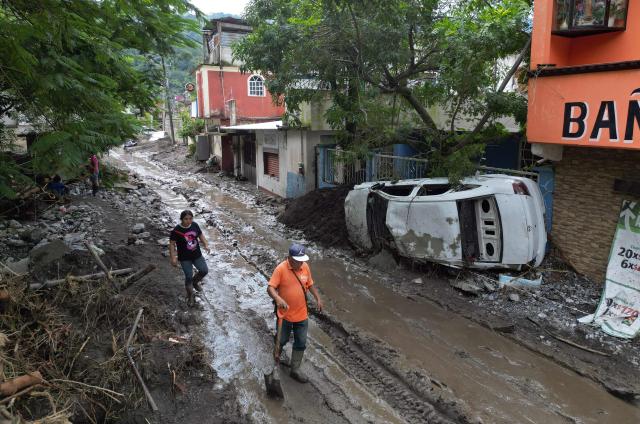 People wade through mud after severe flooding hit the town of Huehuetla in Hidalgo state, Mexico, on October 14, 2025. Rescuers scrambled on October 13, 2025, to reach people cut off by devastating floods that have claimed 64 lives in central and eastern Mexico, with another 65 people reported missing. (Photo by Alfredo ESTRELLA / AFP)