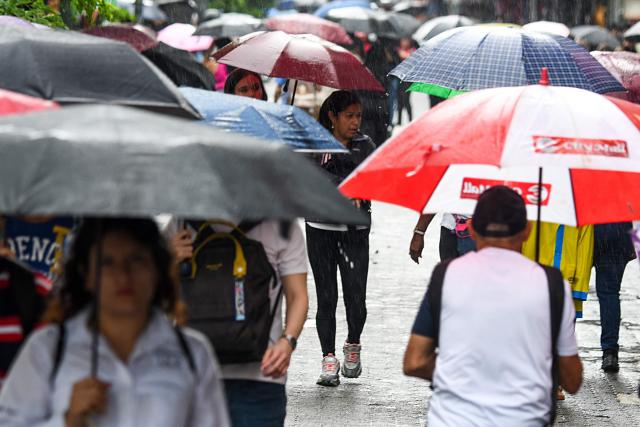 People with umbrellas protect themselves from the rain as they walk on a street in San Jose on October 14, 2025. (Photo by EZEQUIEL BECERRA / AFP)
