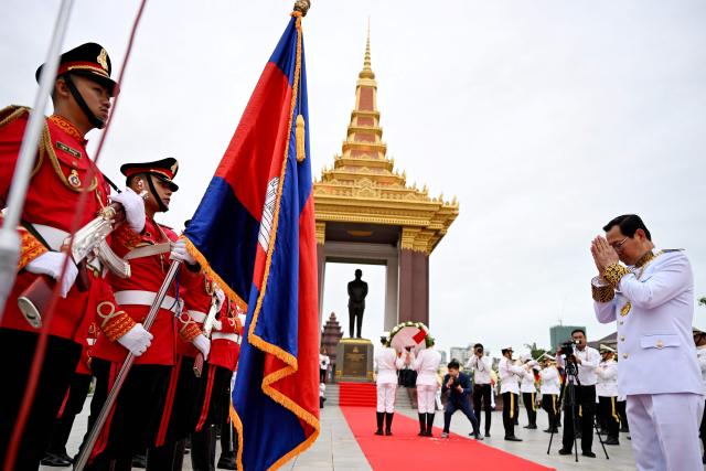 Cambodia's Minister of Justice Koeut Rith (R) gestures to the national flag before paying his respects in front of the monument of the late king Norodom Sihanouk during a ceremony commemorating his thirteenth death anniversary in Phnom Penh on October 15, 2025. (Photo by TANG CHHIN Sothy / AFP)
