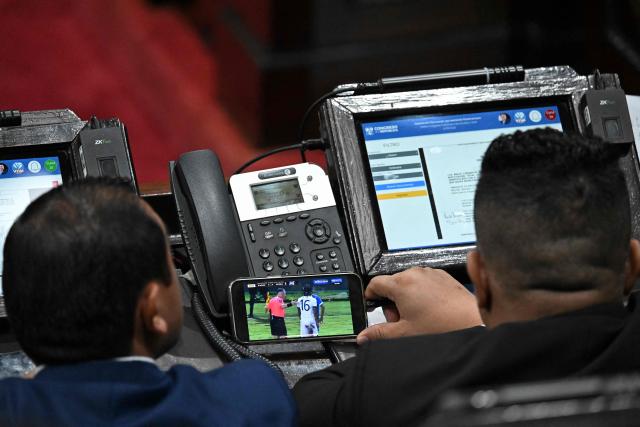 Two deputies watch the football match between the national teams of El Salvador and Guatemala on a mobile phone during a session where they might review and approve an anti-gang law at the National Congress in Guatemala City on October 14, 2025. Twenty members of a gang designated a "foreign terrorist organization" by the United States have escaped from detention in Guatemala, a prison chief said Sunday. (Photo by JOHAN ORDONEZ / AFP)