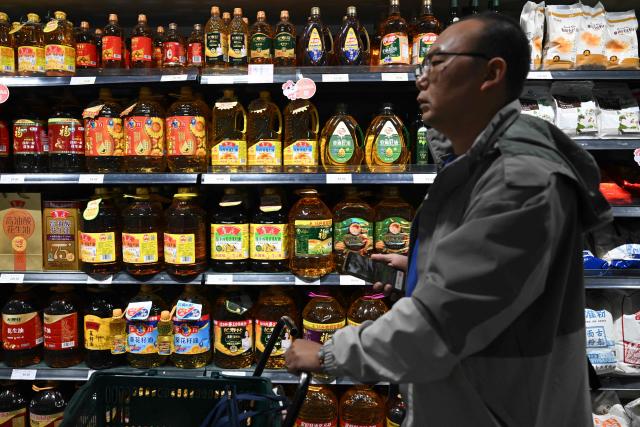 A shopper walks past shelves of cooking oil for sale at a supermarket in Beijing on October 15, 2025. US President Donald Trump slammed China's halt of American soybean purchases as an "economically hostile act," warning October 14 that his country could in turn stop buying cooking oil from the world's second-biggest economy. (Photo by Pedro PARDO / AFP)