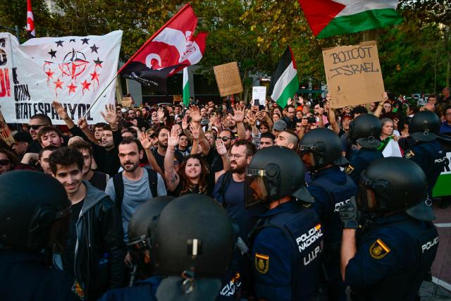 Protesters hold up their arms while facing police during a demonstration against the participation of Israeli basketball team Hapoel IBI Tel-Aviv in the Euroleague, ahead of their match against Valencia Basket, in Valencia, on October 15, 2025. (Photo by Jose JORDAN / AFP)