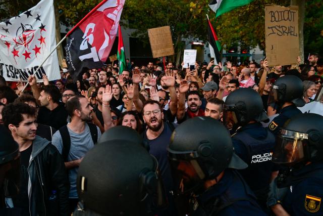 Protesters hold up their arms while facing police during a demonstration against the participation of Israeli basketball team Hapoel IBI Tel-Aviv in the Euroleague, ahead of their match against Valencia Basket, in Valencia, on October 15, 2025. (Photo by Jose JORDAN / AFP)