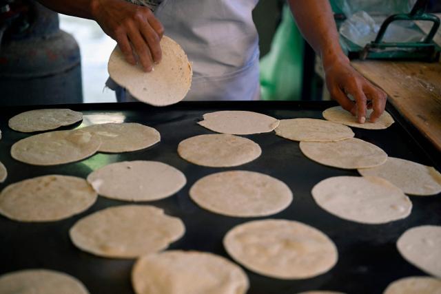 An employee makes tortillas by hand in the town of San Bartolo Tutotepec, Hidalgo state, Mexico on October 15, 2025. In the towns of Mexico hit by last week's deadly rains, tortillas, which are vital to the Mexican diet, particularly in these impoverished areas, are beginning to run out. (Photo by Alfredo ESTRELLA / AFP)