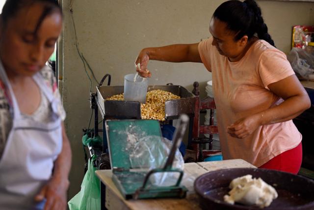 Dulce Esperanza Gomez (R) adds water to corn to prepare dough for making tortillas in the town of San Bartolo Tutotepec, Hidalgo state, Mexico on October 15, 2025. In the towns of Mexico hit by last week's deadly rains, tortillas, which are vital to the Mexican diet, particularly in these impoverished areas, are beginning to run out. (Photo by Alfredo ESTRELLA / AFP)