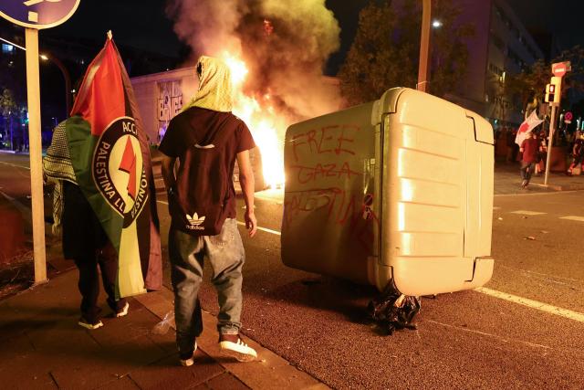 Protesters walk near a burning dumpster which was set alight during a demonstration in support of Palestinians, in Barcelona, on October 15, 2025. Despite the Gaza ceasefire deal signed on October 13, 2025 and a hostage and prisoner exchange between Israel and Hamas, demonstrations in support of the Palestinian people have continued to take place in several Spanish cities. (Photo by Josep LAGO / AFP)