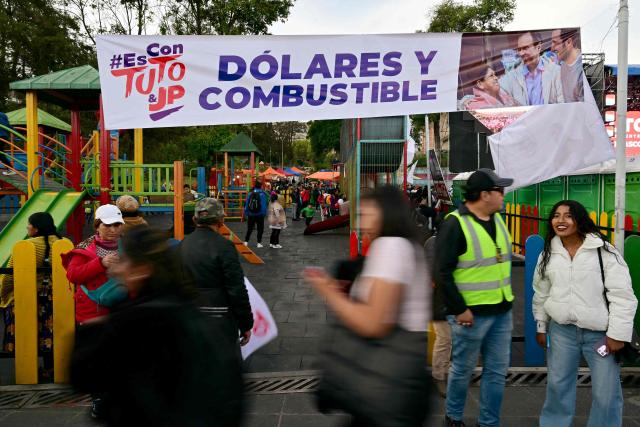 People walk past a banner of Bolivia's presidential candidate for the Freedom and Democracy (Libre) Alliance, Jorge "Tuto" Quiroga during his closing campaign rally in La Paz on October 15, 2025. An ex-president and a senator will go head-to-head in Bolivia's presidential runoff on October 19, 2025, both with promises to fix the South American country's broken economy. Senator Rodrigo Paz came from behind to take the top spot with 32 percent of votes cast in a first round in August, but has since fallen behind ex-president Jorge "Tuto" Quiroga in stated voter intention. (Photo by MARTIN BERNETTI / AFP)