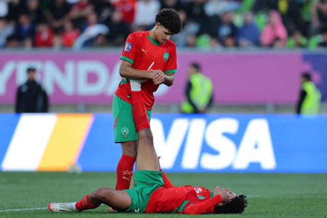 Morocco's defender #4 Ismael Baouf helps teammate defender #3 Ali Maamar stretch his leg muscle during the 2025 FIFA U-20 World Cup semi-final football match between Morocco and France at the Elias Figueroa Stadium in Valparaiso, Chile on October 15, 2025. (Photo by Javier TORRES / AFP)