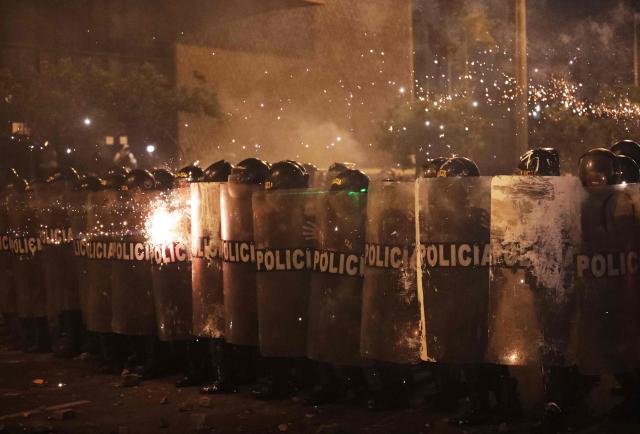 Anti-riot police officers take cover from fireworks as they clash with demonstrators during a protest against Peru's interim President Jose Jeri in Lima on October 15, 2025.  (Photo by CONNIE FRANCE / AFP)