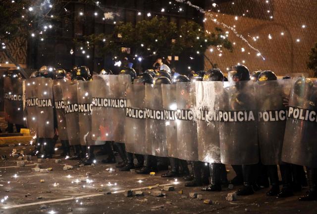 Anti-riot police officers take cover from fireworks as they clash with demonstrators during a protest against Peru's interim President Jose Jeri in Lima on October 15, 2025.  (Photo by CONNIE FRANCE / AFP)