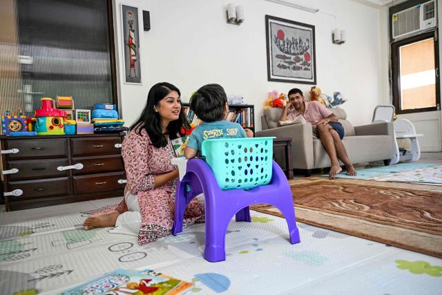 This photograph taken on October 2, 2025 shows Roli Shrivastava (L) and her husband Raman Sankar reading a children's book to their son at their residence in New Delhi. Pollution levels in India's capital city Delhi is shaping decisions on parenthood -- forcing a small yet growing number of people to flee because of the health hazards associated with toxic air. Home to more than 30 million people, New Delhi and the surrounding metropolitan area consistently tops world rankings for air pollution. (Photo by Sajjad HUSSAIN / AFP) / TO GO WITH 'India-Environment-Pollution-Health' FOCUS