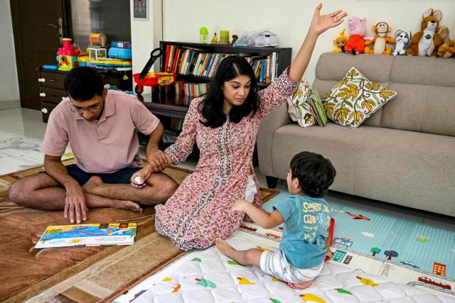 This photograph taken on October 2, 2025 shows Roli Shrivastava (C) and her husband Raman Sankar reading a children's book to their son at their residence in New Delhi. Pollution levels in India's capital city Delhi is shaping decisions on parenthood -- forcing a small yet growing number of people to flee because of the health hazards associated with toxic air. Home to more than 30 million people, New Delhi and the surrounding metropolitan area consistently tops world rankings for air pollution. (Photo by Sajjad HUSSAIN / AFP) / TO GO WITH 'India-Environment-Pollution-Health' FOCUS