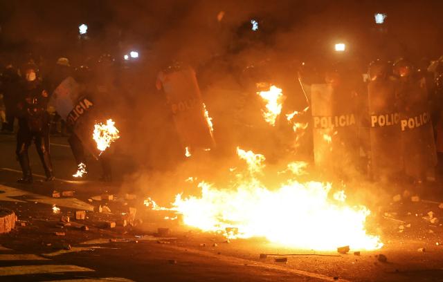 Anti-riot police officers take cover from a fire as they clash with demonstrators during a protest against Peru's interim President Jose Jeri in Lima on October 15, 2025.  (Photo by Hugo CUROTTO / AFP)
