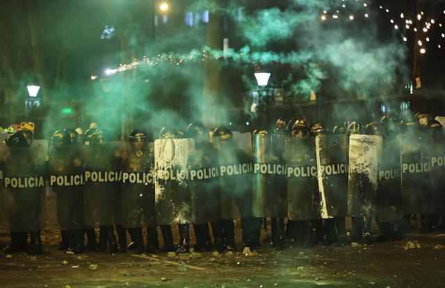 Anti-riot police officers take cover from fireworks as they clash with demonstrators during a protest against Peru's interim President Jose Jeri in Lima on October 15, 2025.  (Photo by Hugo CUROTTO / AFP)