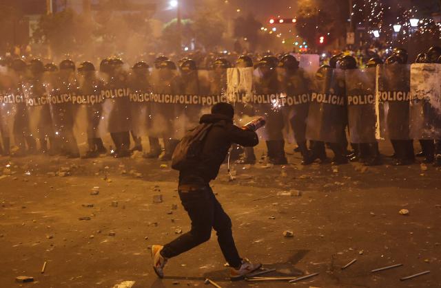 A demonstrator uses fireworks against anti-riot police officers during clashes after a protest against Peru's interim President Jose Jeri in Lima on October 15, 2025.  (Photo by Hugo CUROTTO / AFP)