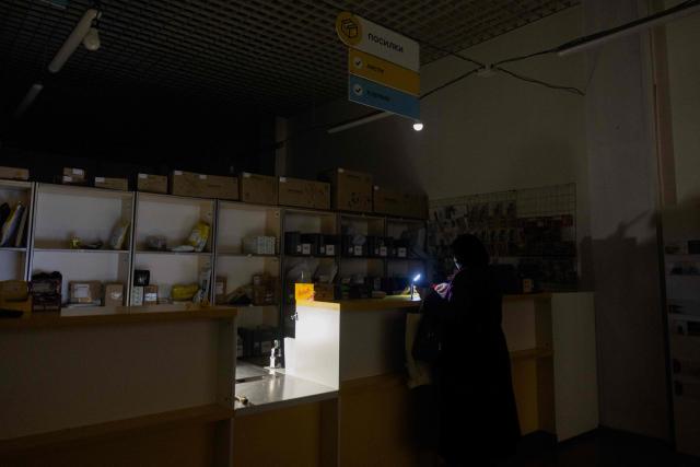 A national postal service of Ukraine worker uses a flashlight to serve a customer during a power outage in Kyiv, on October 16, 2025, amid the Russian invasion of Ukraine. (Photo by Tetiana DZHAFAROVA / AFP)