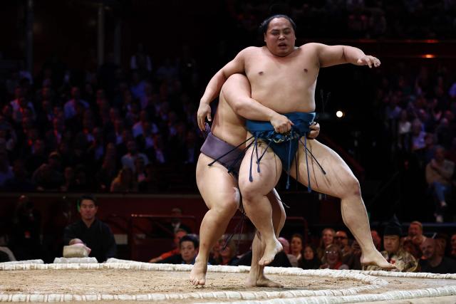 Tobizaru (L) lifts Kotoeiho (R) to win their bout during the Grand Sumo Tournament at the Royal Albert Hall in central London on October 16, 2025. (Photo by HENRY NICHOLLS / AFP)
