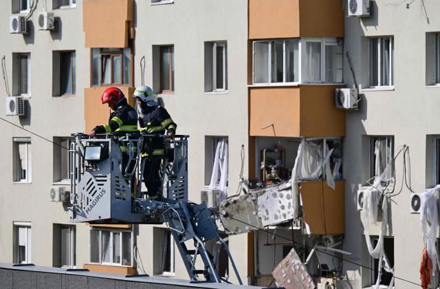 Members of the fire brigade inspect the roof of a school opposite a block of flats were partially destroyed by an explosion in Bucharest, Romania on October 17, 2025. Three people have died and 13 were hospitalized in Romania’s capital Bucharest following a strong explosion on October 17, 2025, according to rescue services. (Photo by Daniel MIHAILESCU / AFP)
