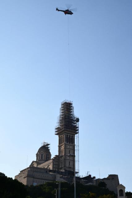 A Puma helicopter airlifts the crown of the Virgin Mari statue sitting atop the Notre Dame de la Garde Basilica, known to locals as Bonne Mère (The Good Mother), in Marseille on October 17, 2025, during its reinstallation following restoration works on the crown. (Photo by Christophe SIMON / AFP)