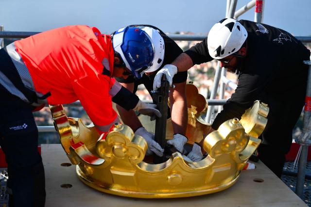 TOPSHOT - Technicians reinstall the crown of the Virgin Mari statue sitting atop the Notre Dame de la Garde Basilica, known to locals as Bonne Mère (The Good Mother), in Marseille on October 17, 2025, following restoration works. (Photo by Christophe SIMON / AFP)
