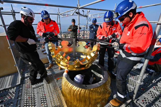 TOPSHOT - Technicians reinstall the crown of the Virgin Mari statue sitting atop the Notre Dame de la Garde Basilica, known to locals as Bonne Mère (The Good Mother), in Marseille on October 17, 2025, following restoration works. (Photo by Christophe SIMON / AFP)