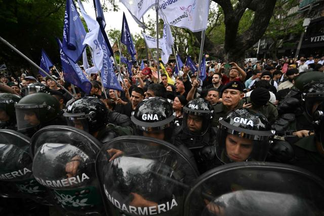 Supporters of Argentina's President Javier Milei stand behind a line of gendarmerie officers as opponents demonstrate before his arrival for a campaign rally in Buenos Aires, on October 17, 2025, ahead of the upcoming legislative elections. Milei, once a global poster boy for budget-slashing libertarian politics, is heading into the polls diminished by his failure to stabilize Argentina's ailing peso despite spending nearly all the Central Bank's dollar reserves to prop it up. (Photo by Luis ROBAYO / AFP)